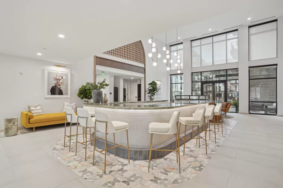 Curved bar with white stools, pendant lights, and modern seating in bright, airy lounge.