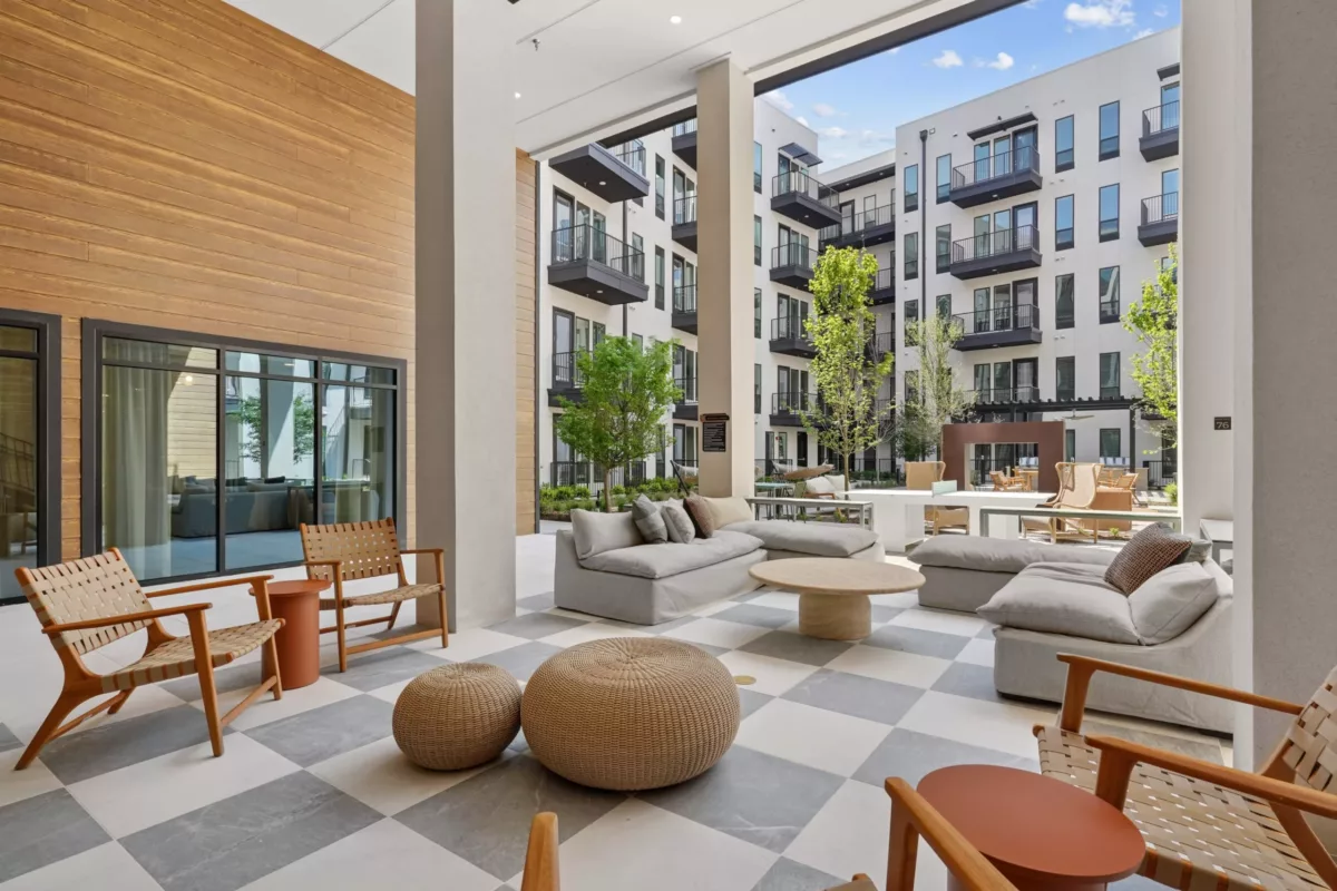 Covered patio with cushioned seating, checker tile, and courtyard backdrop.