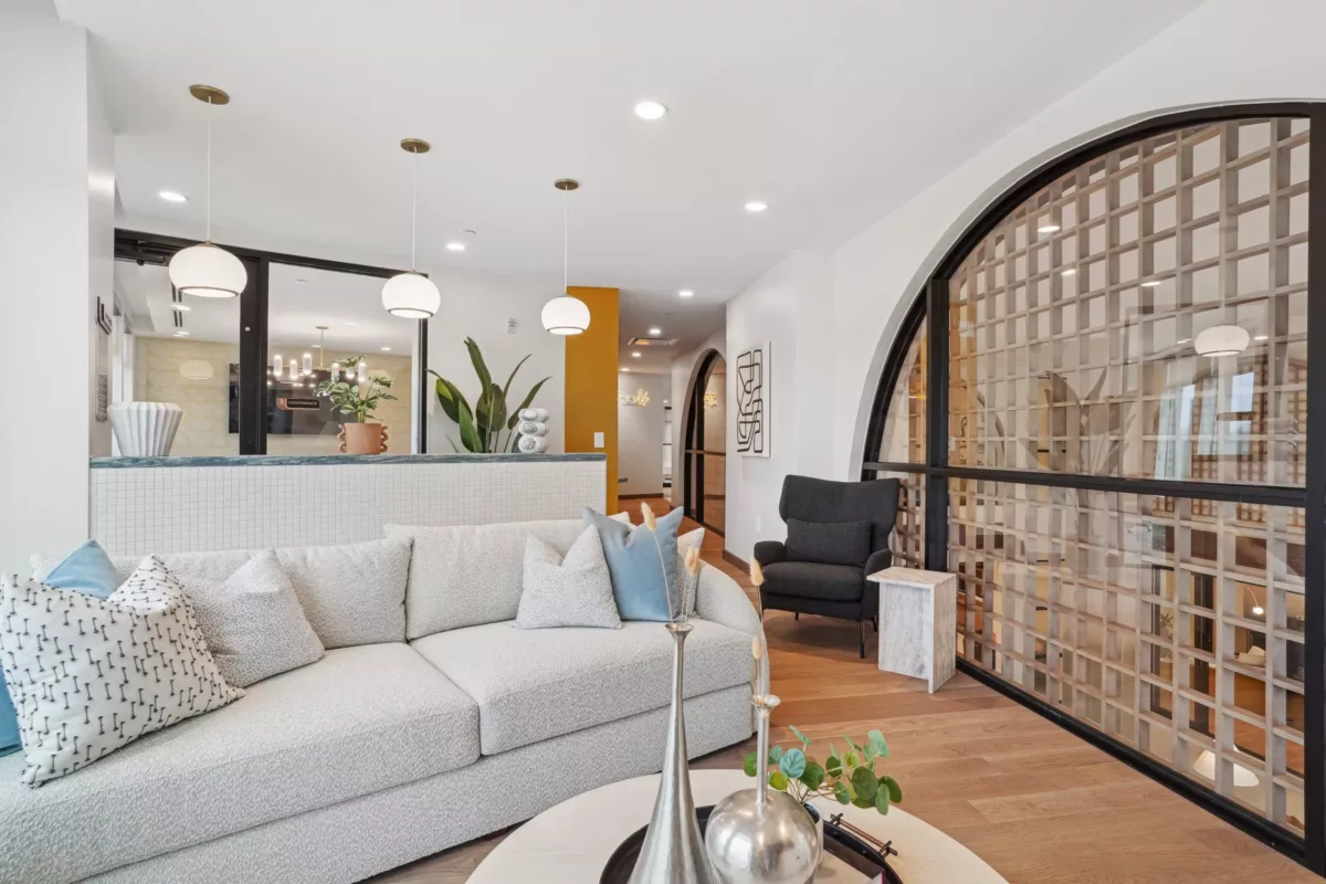 Coworking lounge with plush white sofa, modern lighting, and arched glass partition.