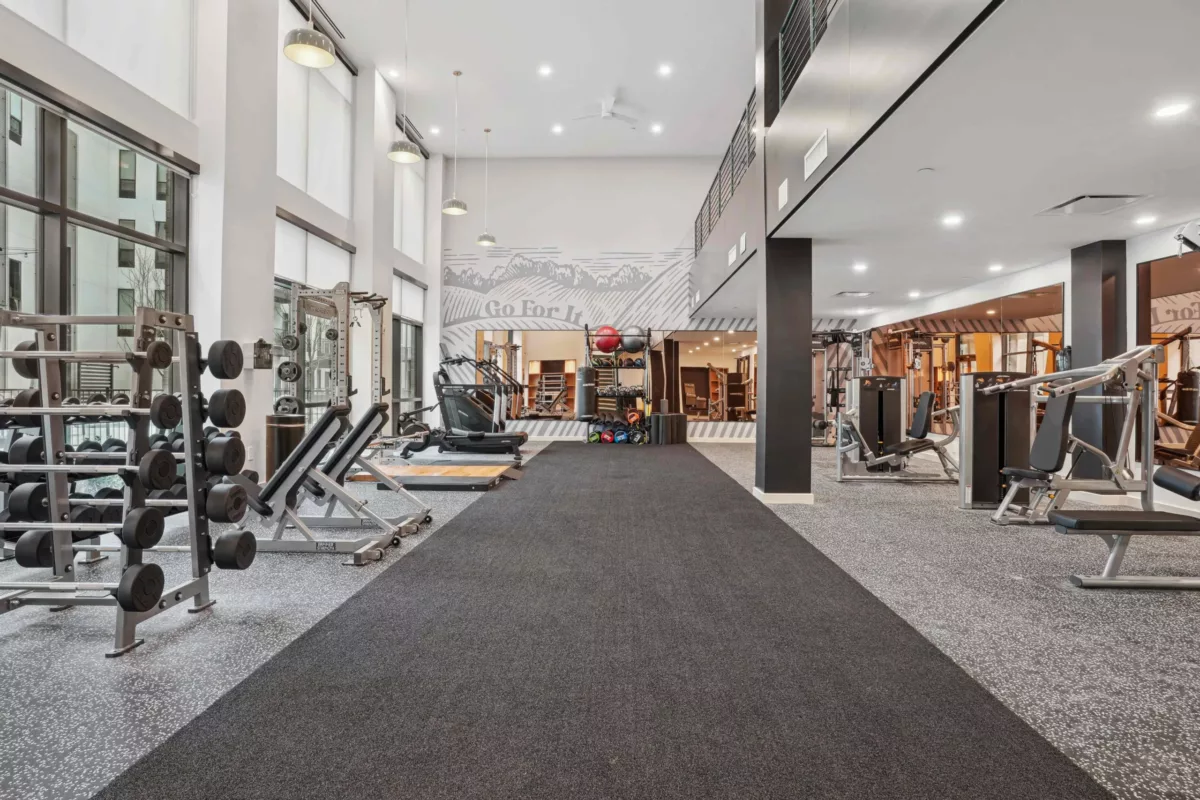 Open-concept gym with weight racks, machines, and high ceilings with windows.