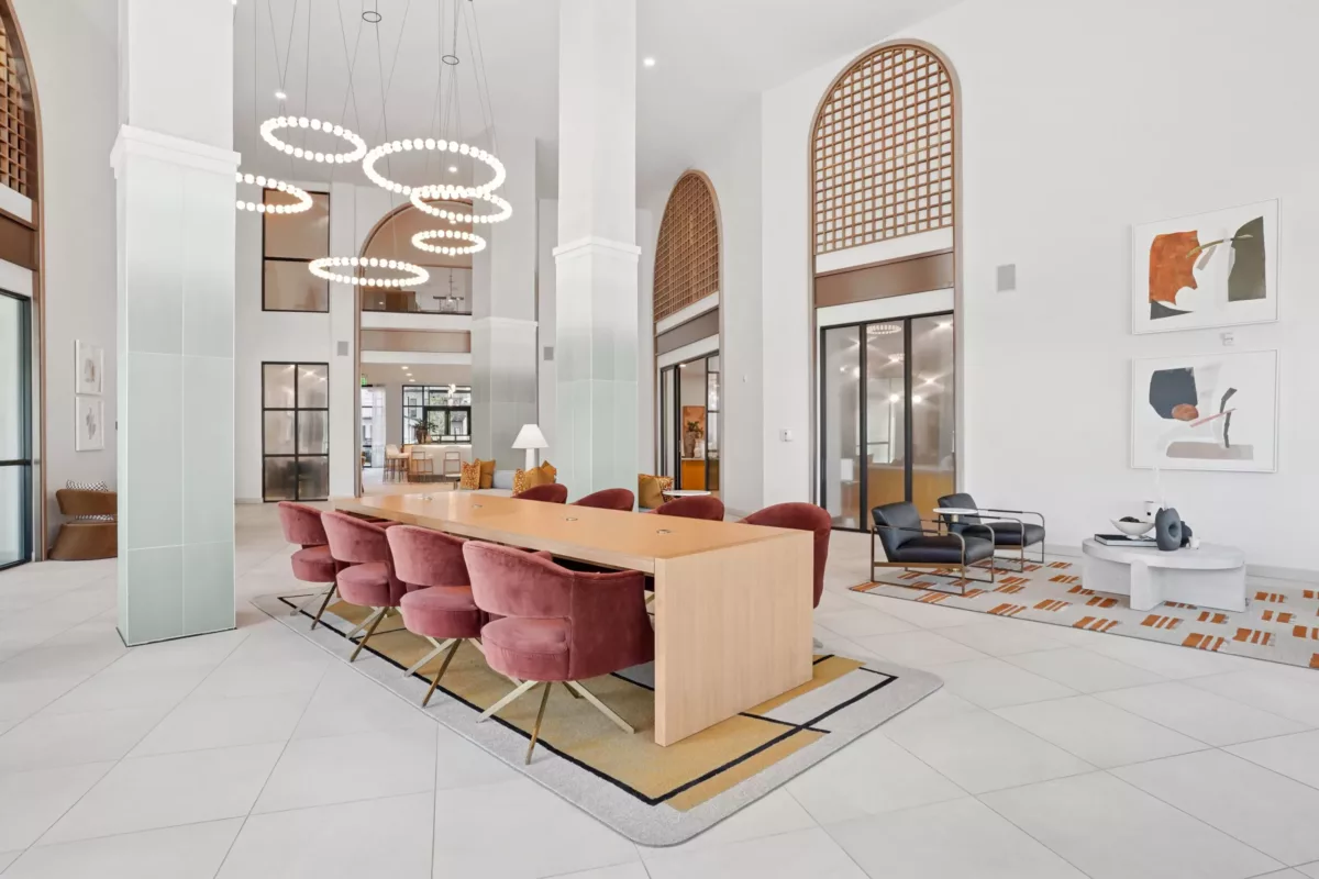 Tall-ceilinged lobby with pink chairs, wood table, and circular light fixtures.