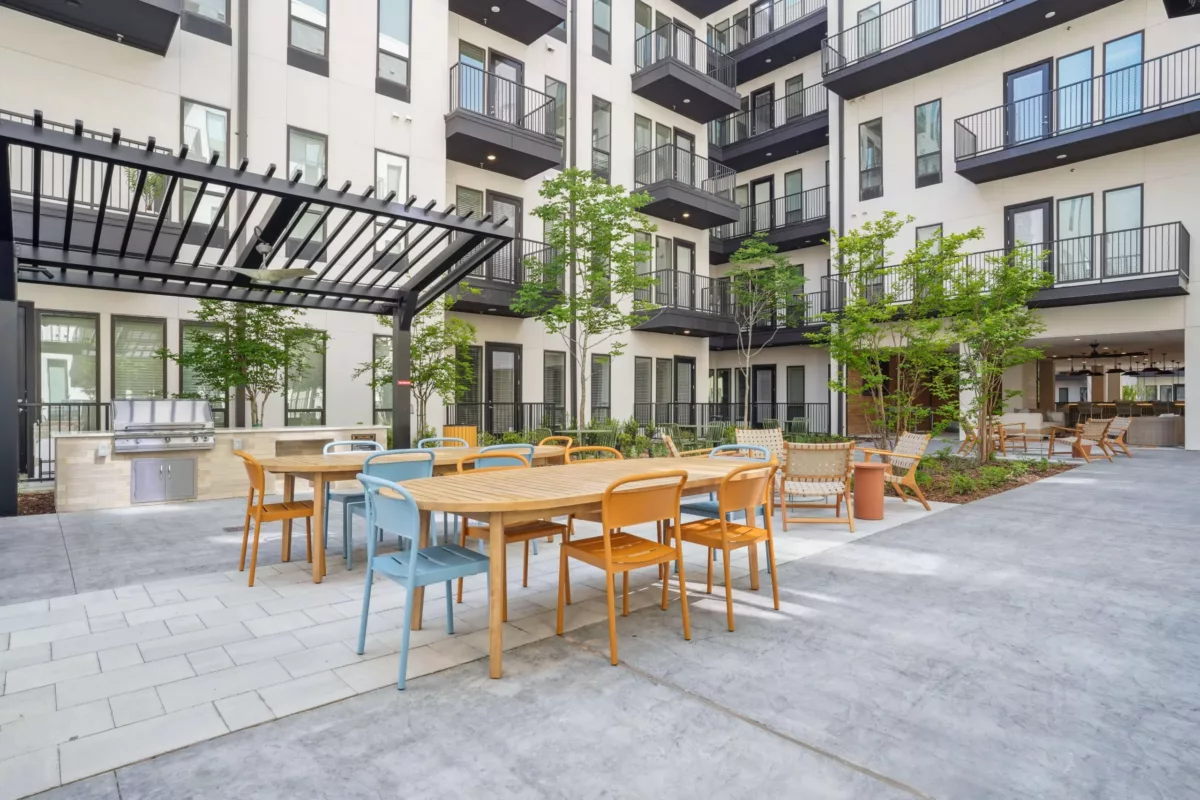 Courtyard dining area with grill station, colorful chairs, and pergola cover.