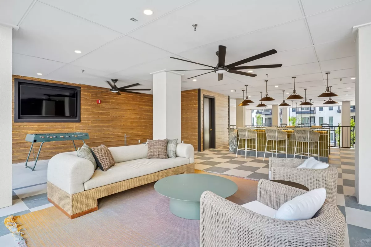 Outdoor lounge with wicker seating, TV, foosball, and bar seating under fans.