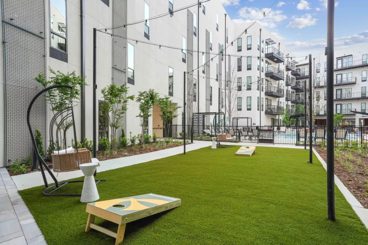 Grassy game area with cornhole boards, string lights, and swing chairs.