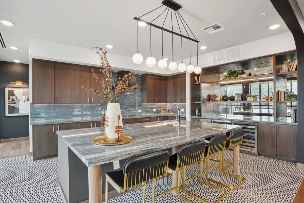Modern community kitchen with marble island, pendant lighting, and gold-accented barstools.