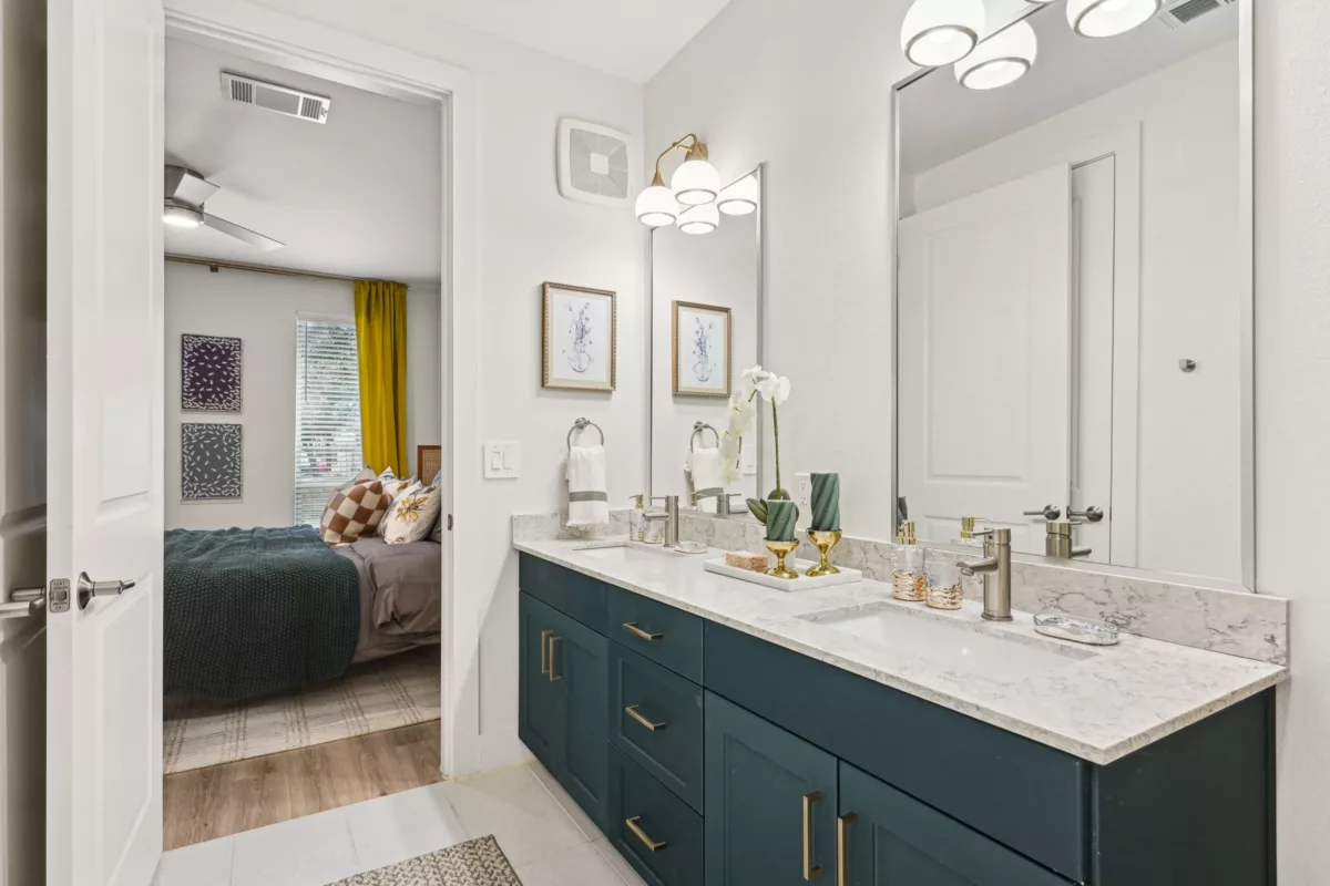 Double-sink bathroom with marble counters, gold fixtures, and a view into the bedroom.