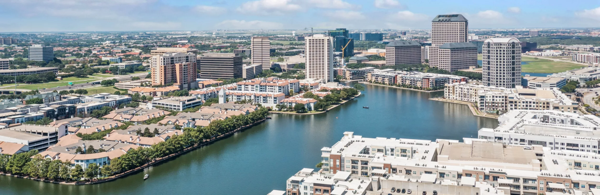 Aerial view of a city with buildings, a lake, and surrounding greenery.
