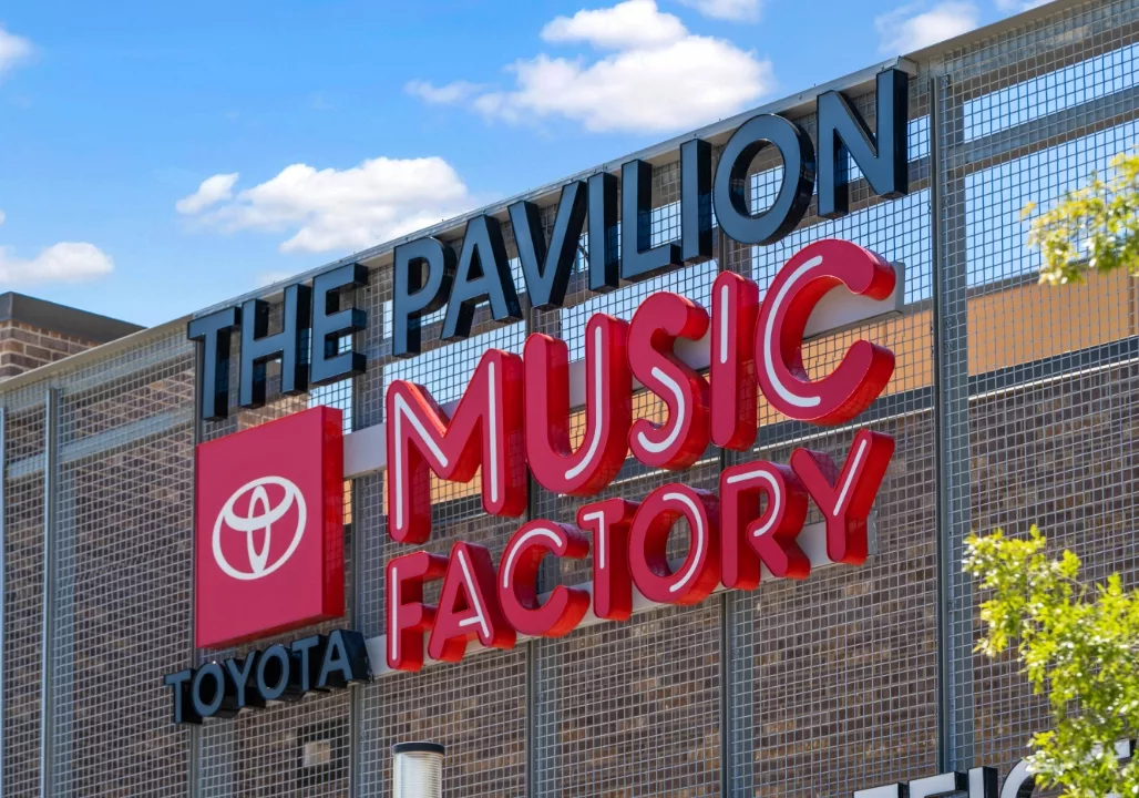 "The Pavilion Toyota Music Factory" sign on a metal structure against a blue sky.