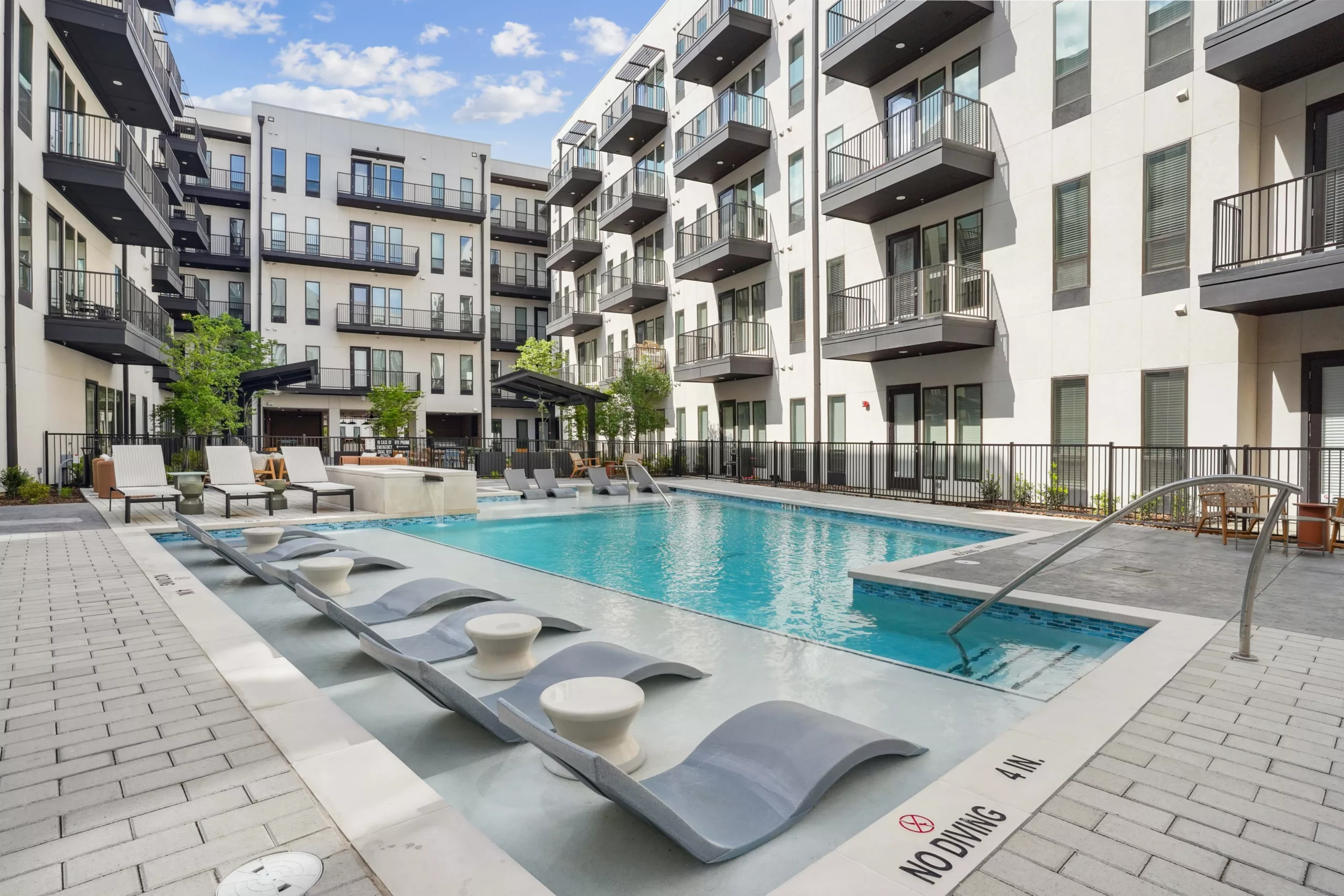 Outdoor pool with in-water loungers, surrounded by modern apartment balconies.