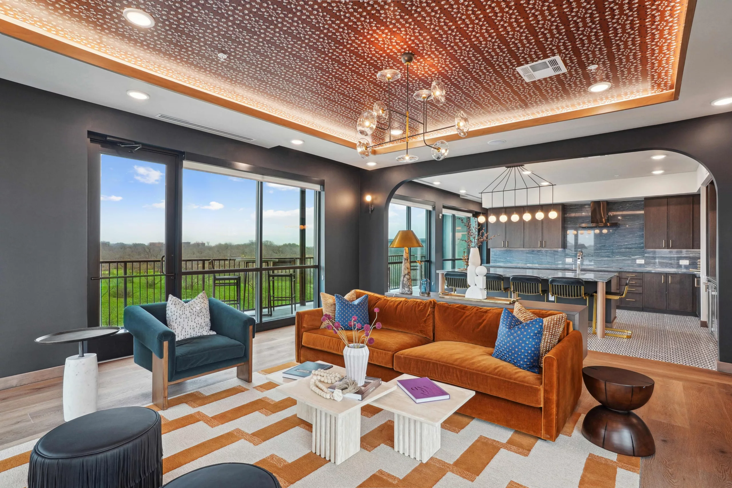 Stylish lounge with a patterned ceiling, moden light fixture, velvet sofa, modern decor, and bar seating overlooking greenery.
